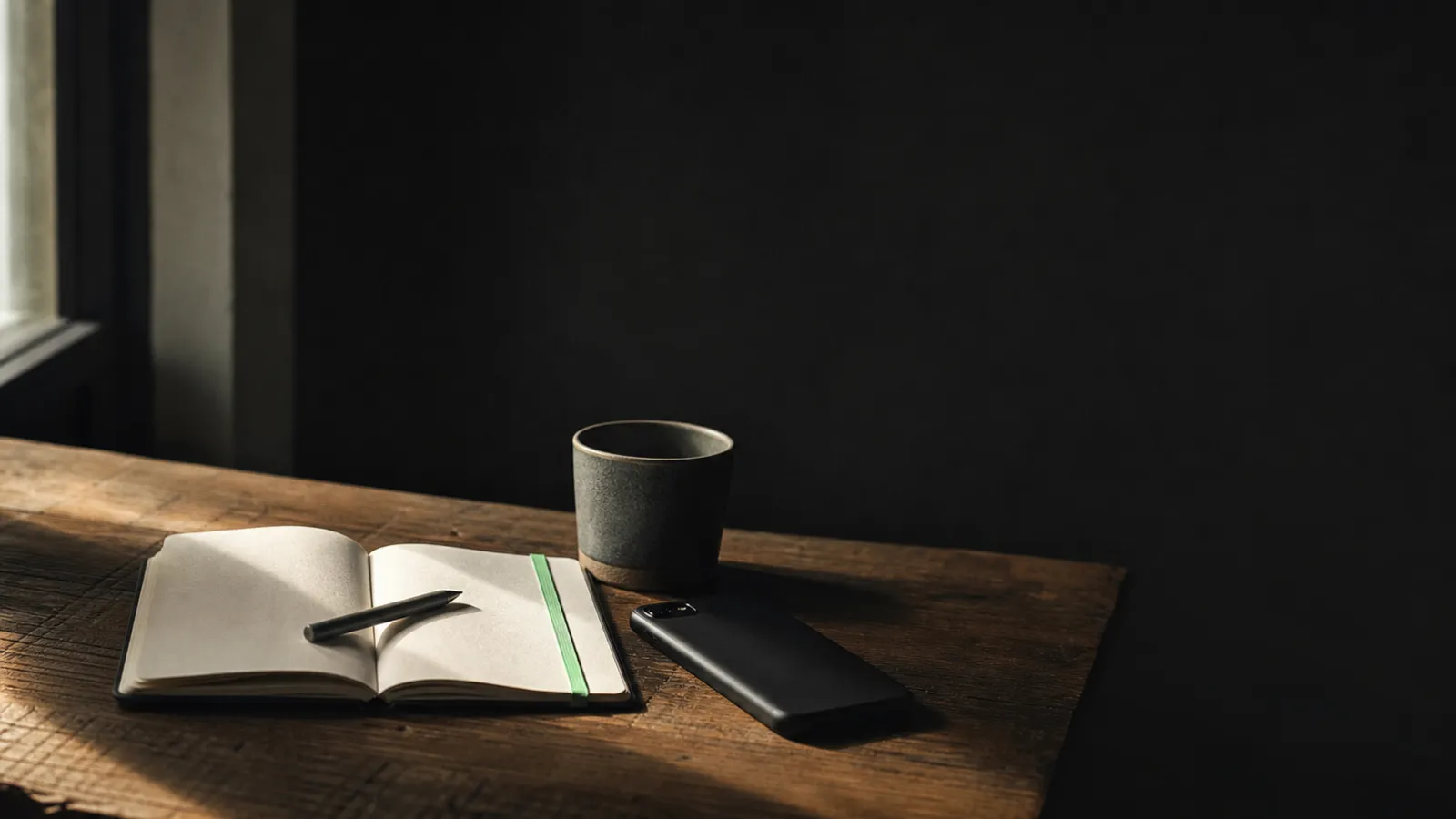 A notebook, pen and coffee beside a phone on a dark desk, set up for aesthetic clinic marketing planning