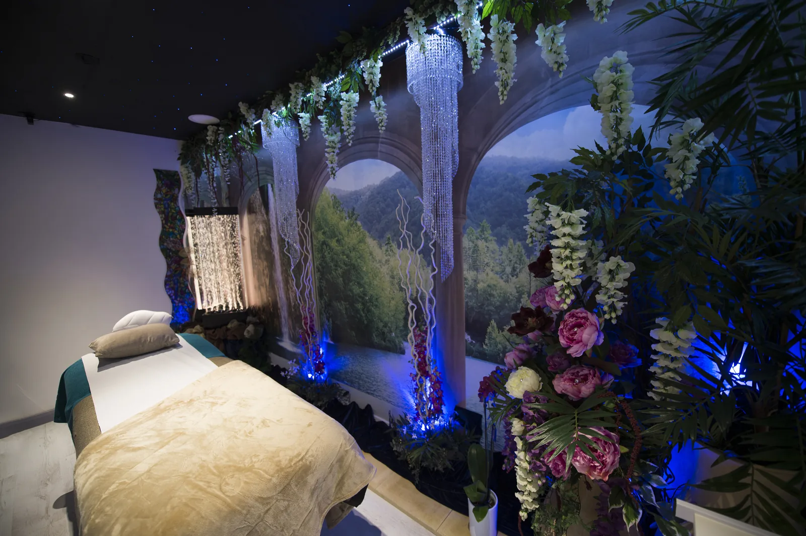 A themed aesthetic treatment room with a scenic wall mural, crystal chandeliers, a star-lit ceiling and florals