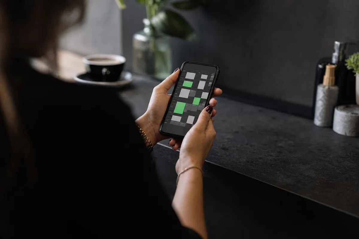 Salon owner's hand holding a phone showing a booking calendar at the reception desk