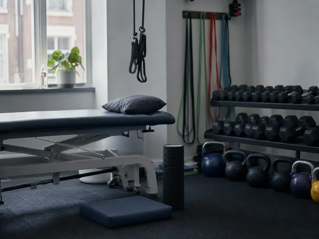 A sports injury clinic with a treatment plinth, a rack of kettlebells and resistance bands on a wall rail
