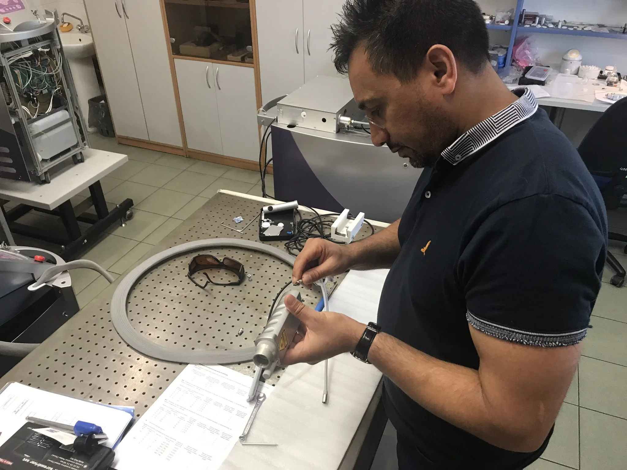 Surinder Ahitan dismantling a fibre-optic laser handpiece at a workbench.